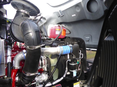 Mack MD6 engine bay with intercooler piping, red coolant reservoir, blue hose, and various hoses and components visible.