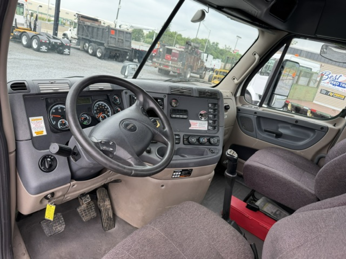 Dashboard and steering wheel of a 2017 Freightliner Cascadia daycab interior; visible gauges, steering wheel, center console, driver's seat, passenger seat, door panel, and pedals.