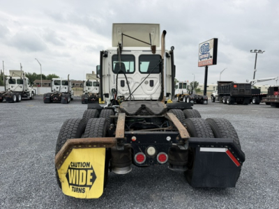 Truck rear view of a 2017 Freightliner Cascadia CA125DC showing fifth wheel/hitch and dual rear axles with yellow 'Caution Wide Turns' mudflap and tool/storage box.