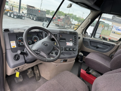 Dashboard and steering wheel of a 2017 Freightliner Cascadia daycab interior; visible gauges, steering wheel, center console, driver's seat, passenger seat, door panel, and pedals.