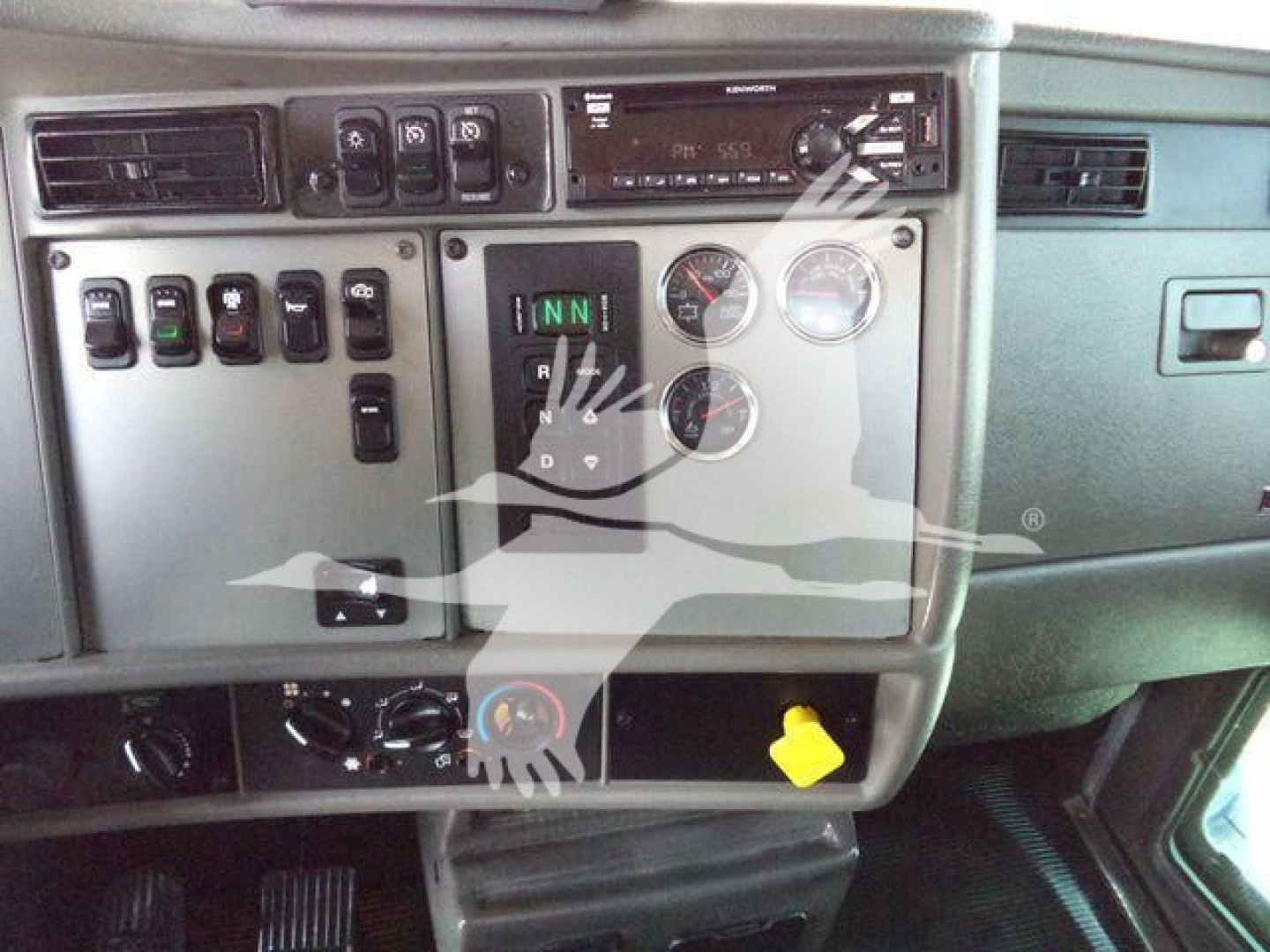 Kenworth T370 dashboard/console showing gear selector with position indicators and multiple gauges; various switches and a CD player head unit visible.
