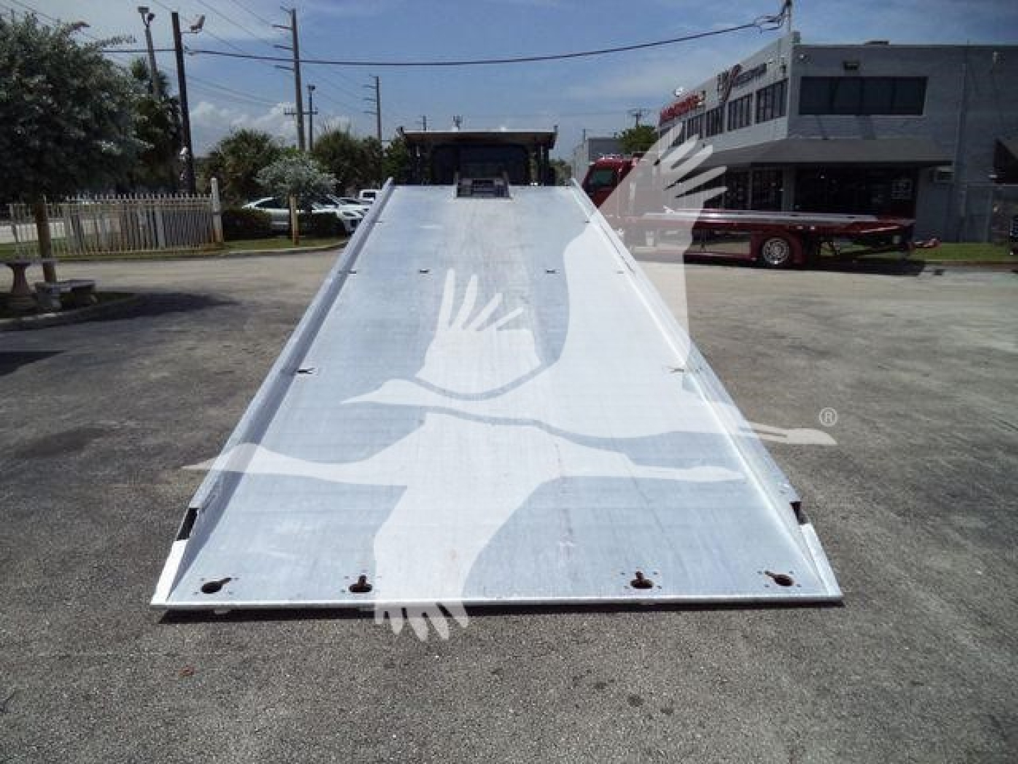 Flatbed tow truck bed on a 2016 Kenworth T370, aluminum surface with hinge at rear and bolts along edges, viewed from the front of the ramp.