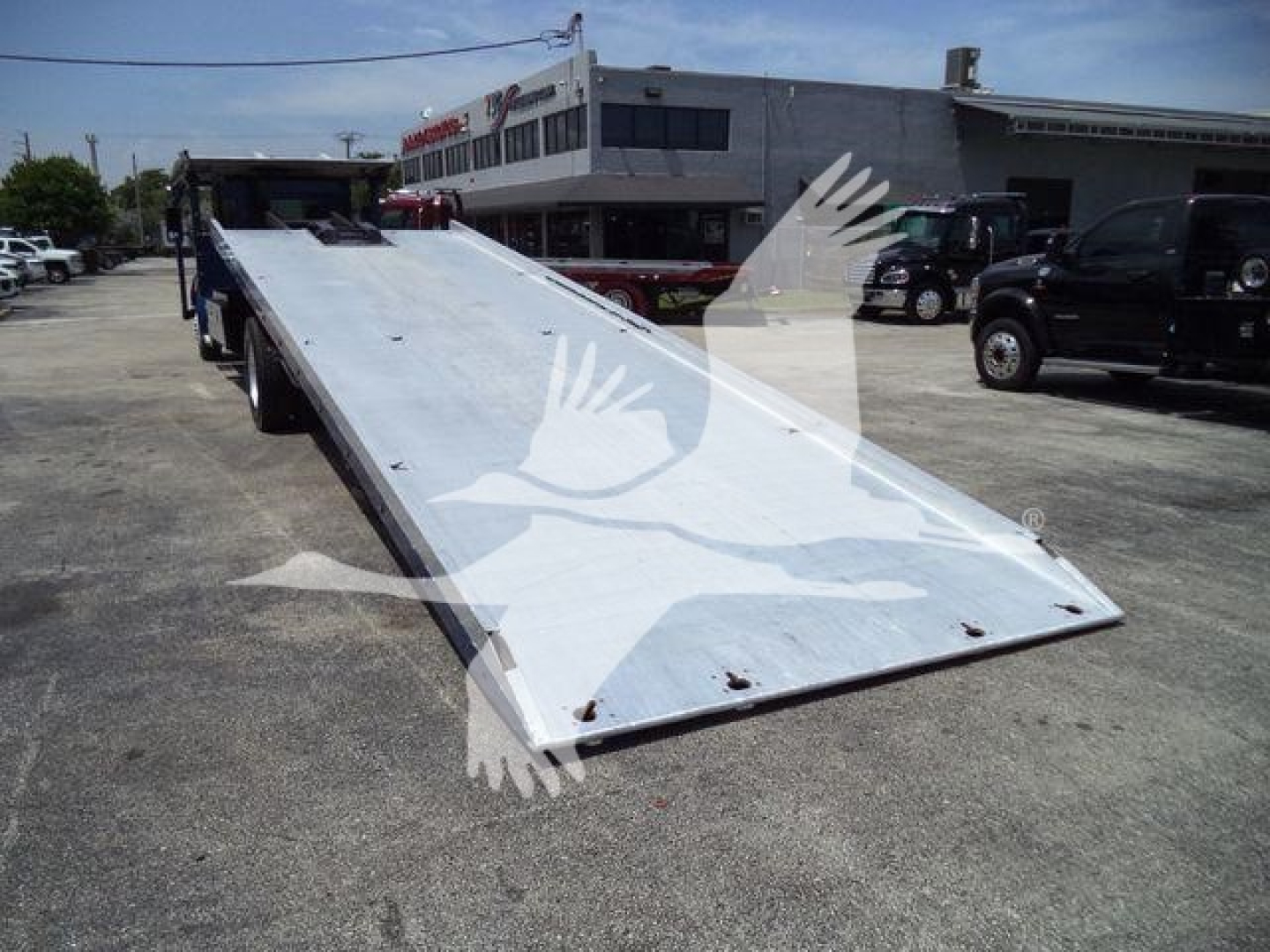 Kenworth T370 rollback flatbed truck and ramp in a dealership lot.
