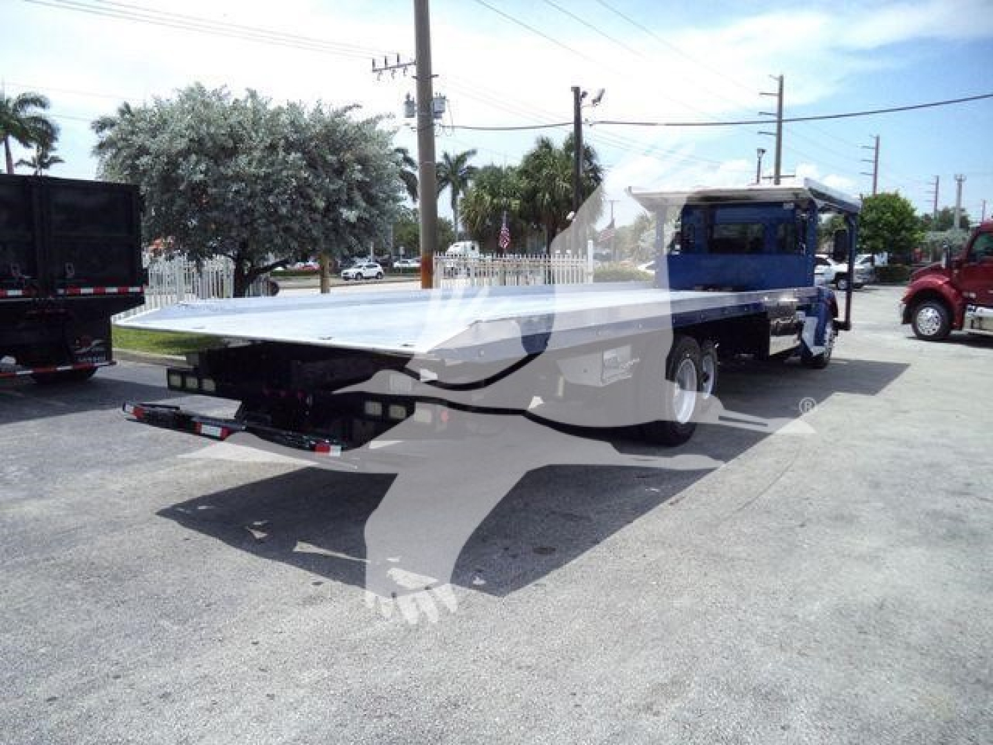 Kenworth T370 rollback tow truck with flatbed, blue cab, silver bed, in a dealership lot.