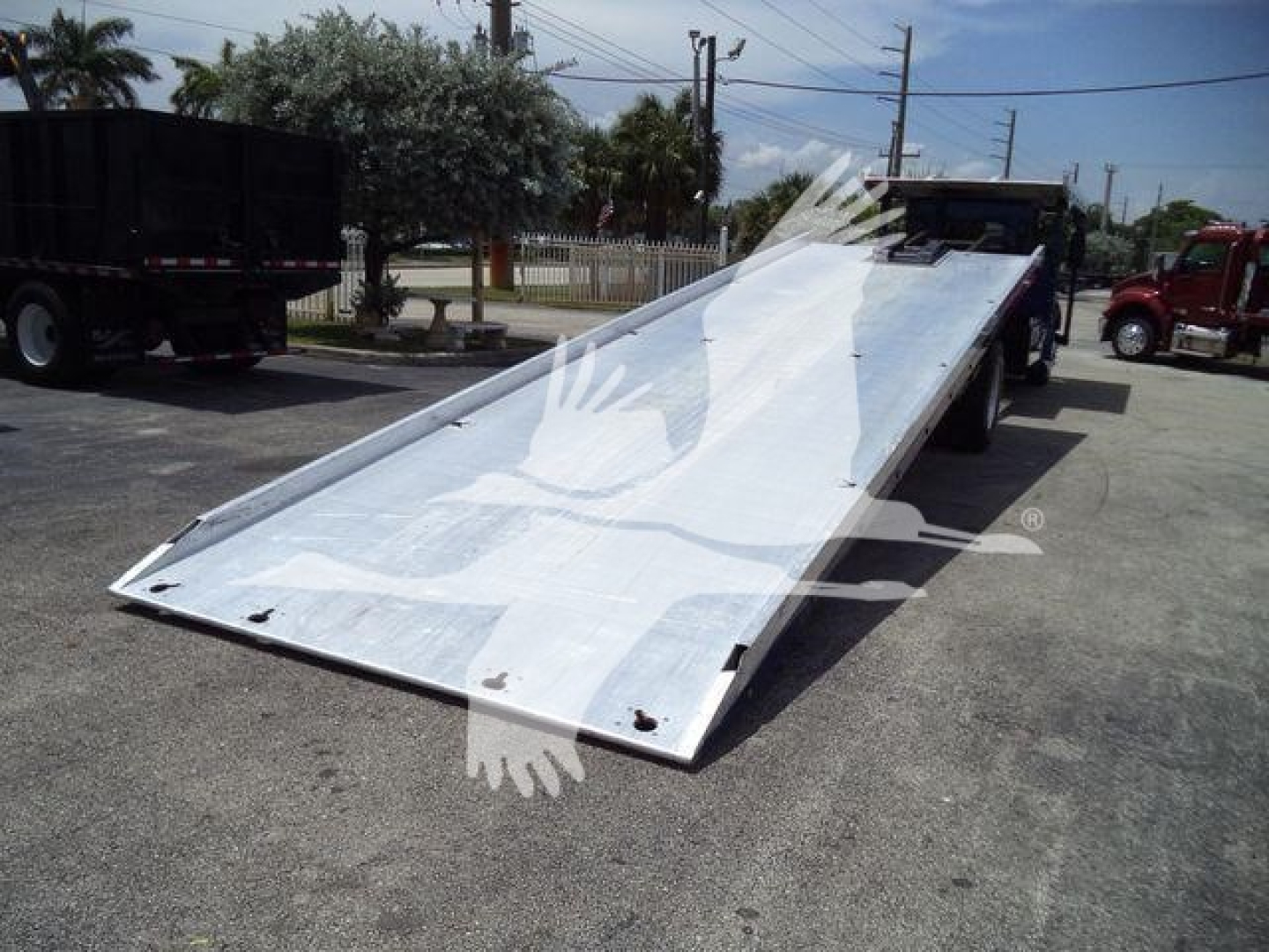 Kenworth T370 rollback truck with a lowered aluminum ramp bed, side rails, and cab in background.