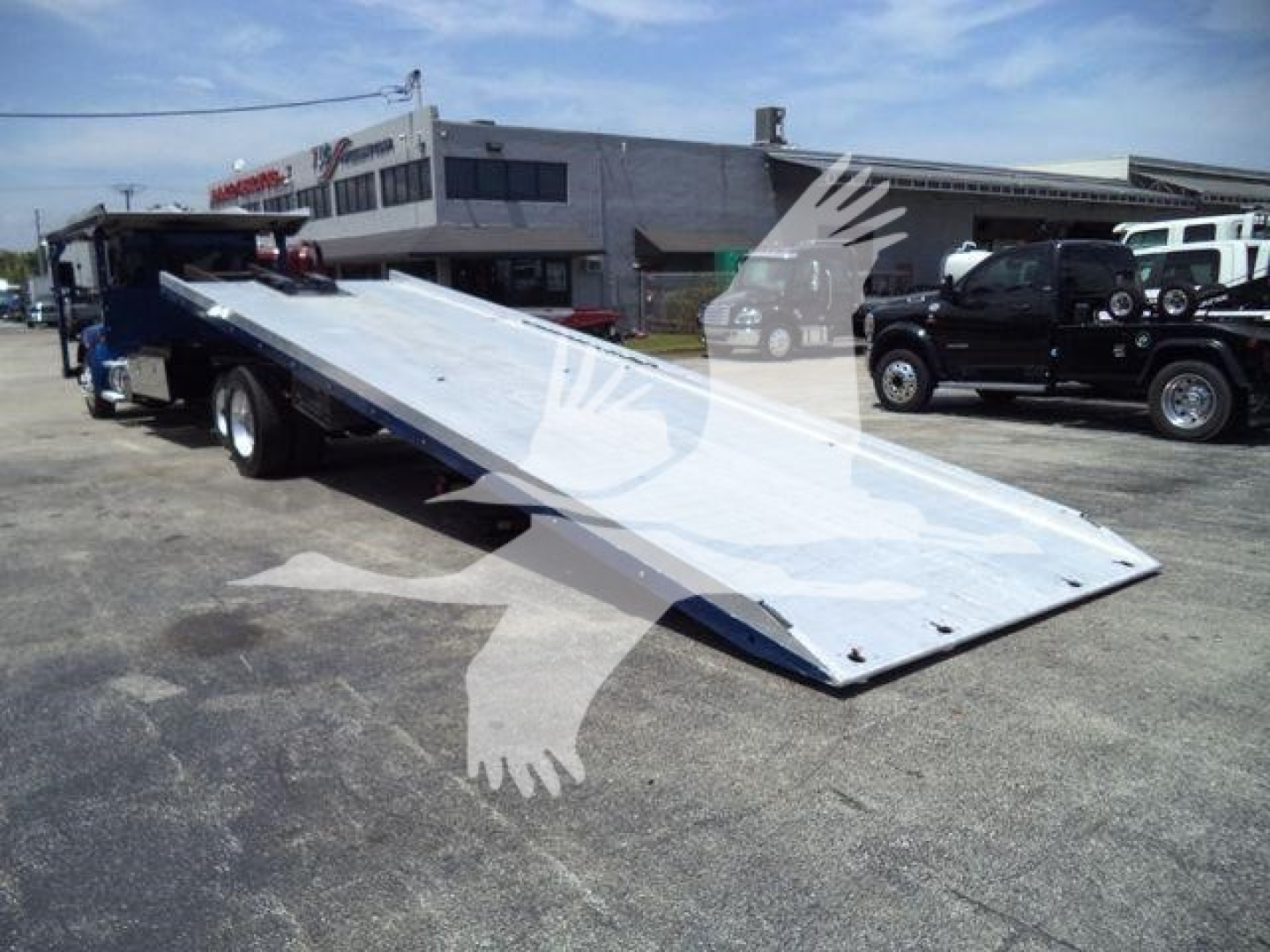 Kenworth T370 rollback tow truck with a lowered front ramp, metal deck and towing equipment in a dealership lot