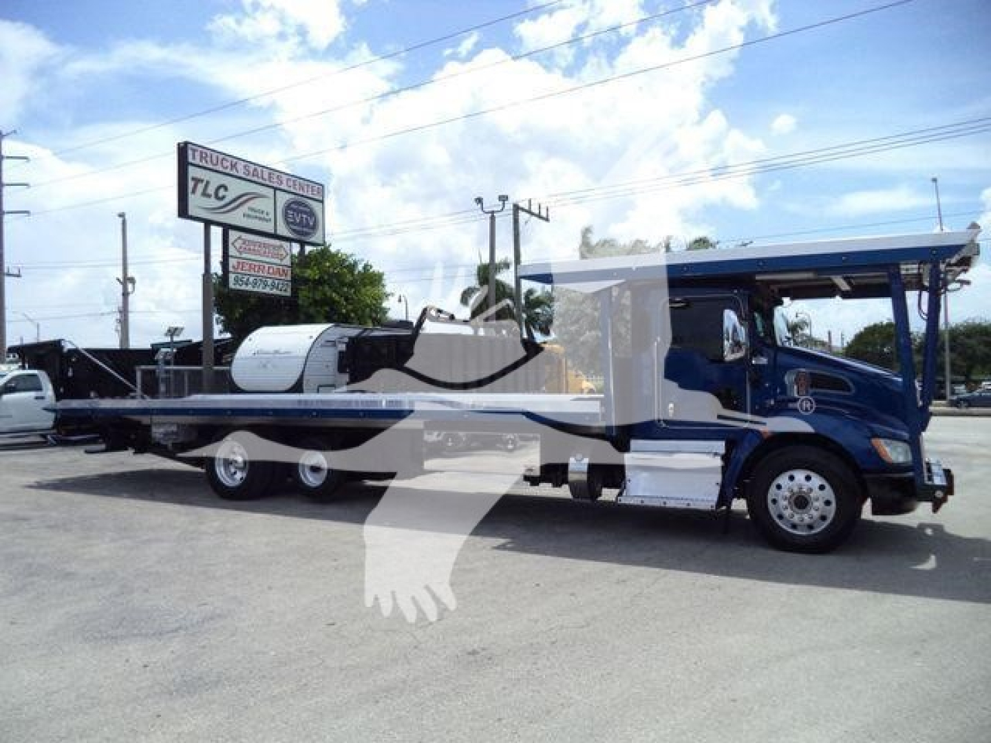 Kenworth T370 rollback tow truck with long flatbed, blue cab, white accents, extended chassis, parked at a lot.