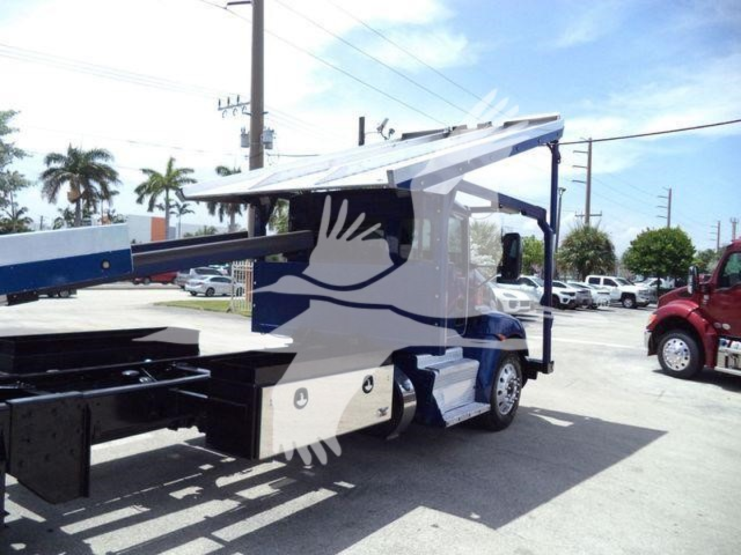Kenworth T370 rollback truck in a yard with a hydraulic bed extended; cab white with blue accents and logo; rear chassis visible