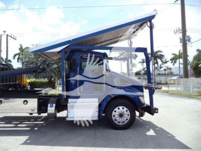 Truck side view of a 2016 Kenworth T370 rollback with a raised blue and white bed, cab doors, chrome wheels, and hydraulic lift components visible.