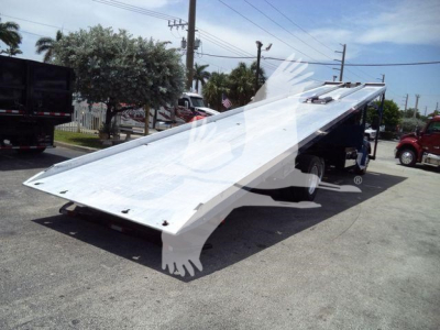 Truck rollback bed tilted upward showing aluminum deck and ramps with Kenworth T370 equipment in a dealership lot.