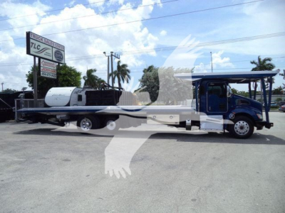 Kenworth T370 rollback truck with a long flatbed and rear wheel lift, blue cab, black and white equipment, visible signboards in background.