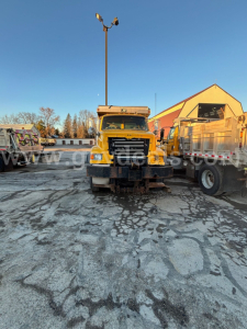 Front view of a yellow 2007 Sterling L8500 dump truck in a lot with other trucks and industrial buildings.