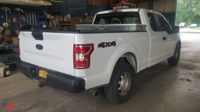 2016 Ford F-150 pickup truck 4x4 rear-quarter view in a workshop showing cargo bed and tailgate with Ford badge