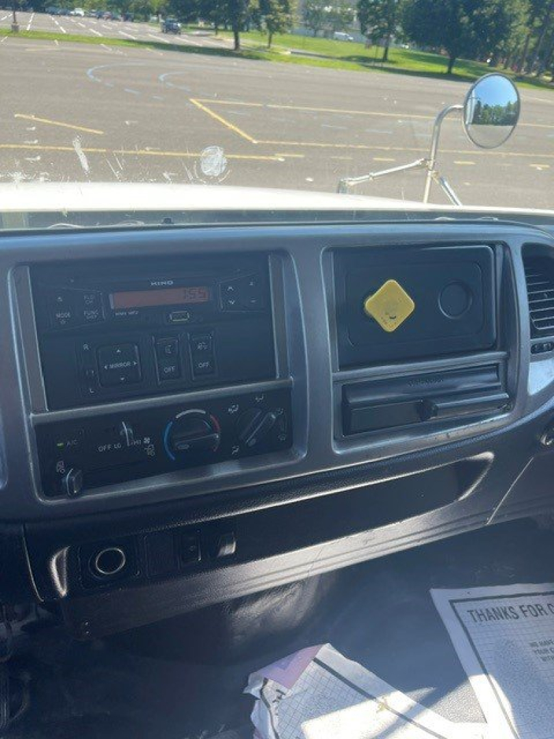 Dashboard view of a 2015 Hino 338 cab with steering wheel, radio, climate controls, and a yellow caution tag on the glove box.