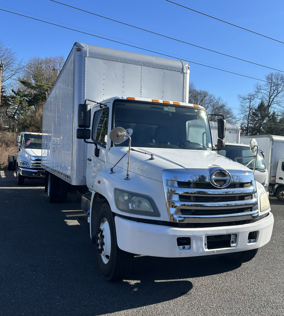 Hino 338 box truck in view showing cab and large cargo box, front chrome grille, headlights, side mirrors, and orange clearance lights.