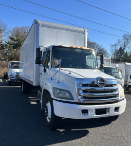 Hino 338 box truck in view showing cab and large cargo box, front chrome grille, headlights, side mirrors, and orange clearance lights.