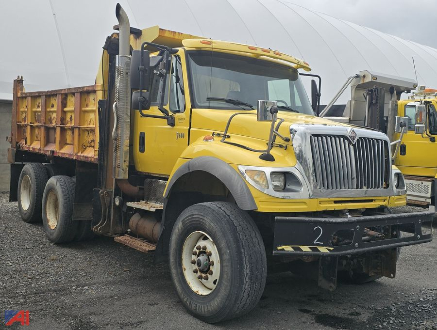 1995 International WorkStar 7600 dump truck in yellow with a heavy-duty front grille, dual front wheels, and a dumping box. The truck is on a dirt surface with a white tent in the background.