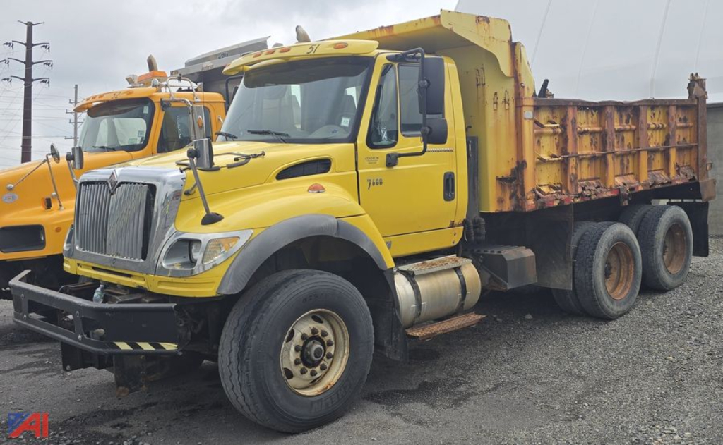 2005 International WorkStar 7600 dump truck in yellow with rusted dump bed, front grille and headlights visible, two-axle front, three-axle rear, black bumper.