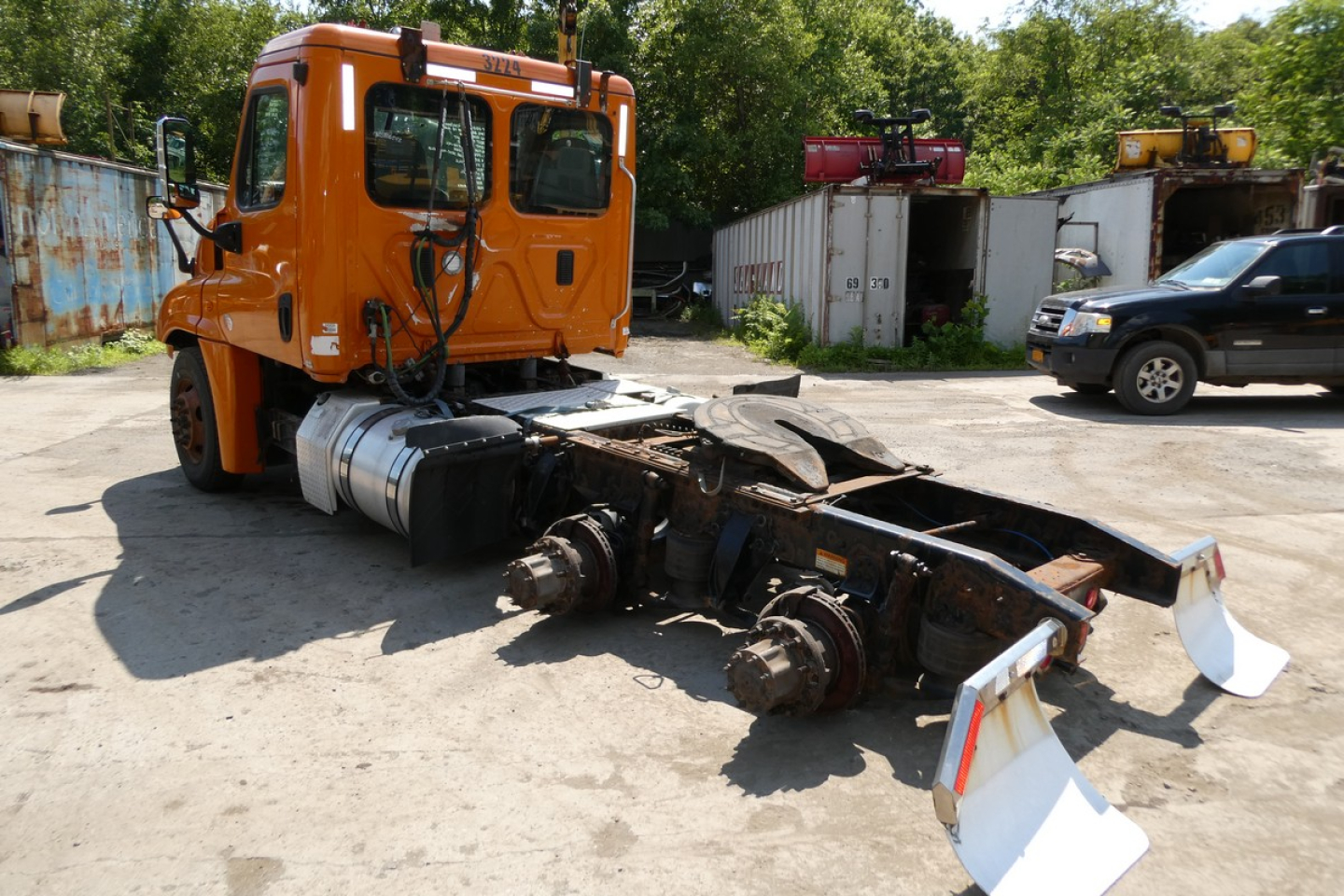 Orange Freightliner Cascadia 125 cab over truck chassis with exposed drive train and landing gear in an outdoor yard.
