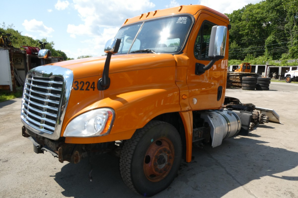 Orange Freightliner Cascadia 125 daycab truck in a yard, side view showing cab, front grille, and wheels; VIN and stock number not visible in this view.