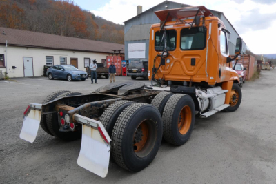 Orange Freightliner Cascadia 125 daycab tractor rear angle showing chassis, dual rear axles, and mud flaps.
