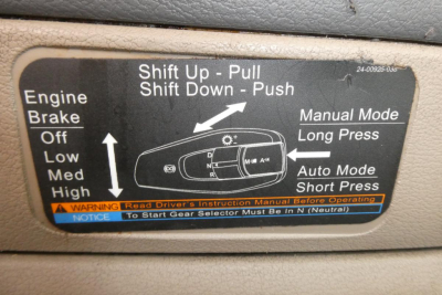 Label showing shift control instructions and gear lever positions in a Freightliner Cascadia 125 cab; text includes Shift Up - Pull, Shift Down - Push, Manual Mode Long Press, Auto Mode Short Press, warning and driver instruction notes