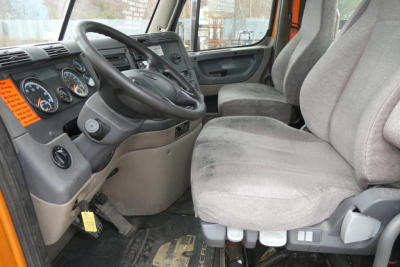 Cab interior of Freightliner Cascadia 125 daycab showing steering wheel, dashboard gauges, and grey fabric seats.