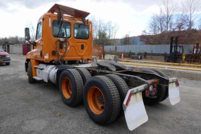 Orange Freightliner Cascadia 125 daycab tractor rear view with triple rear axles and mudflaps.