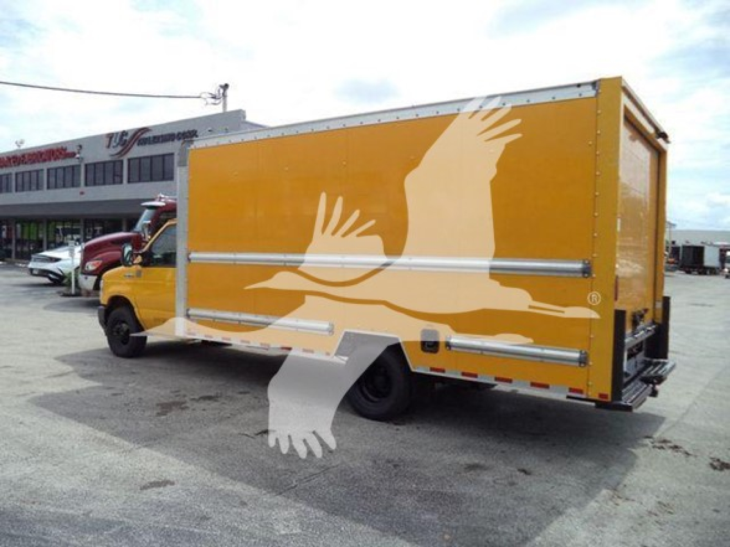Ford E-350 box truck rear and side view showing yellow cargo body with white dove graphic and silver trim, side step, and rear bumper