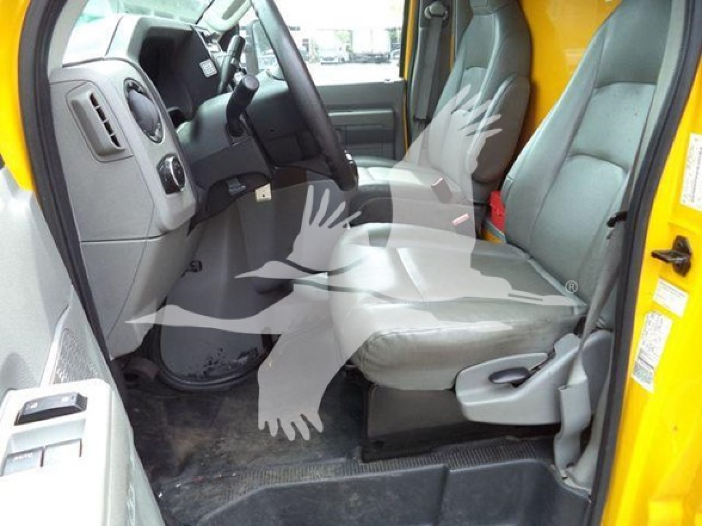 Ford E-350 cargo van interior showing front seats and driver area, grey seats, steering wheel, clutch pedal, and floor mats; yellow exterior visible at edge.