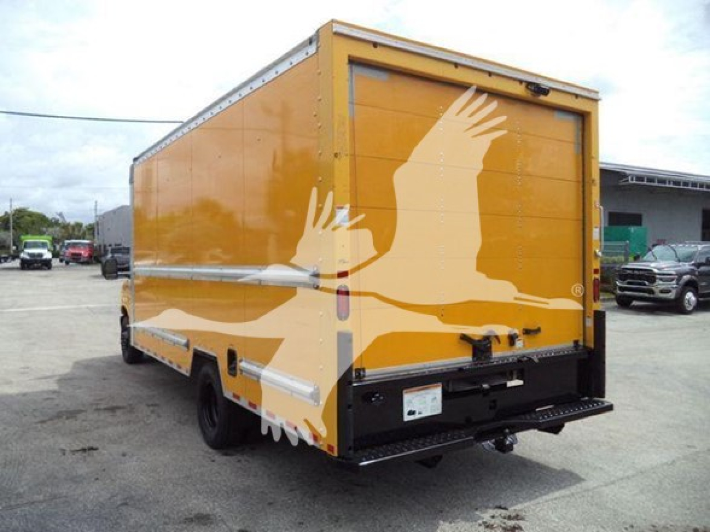 Rear-side view of a yellow Ford E-350 XL SD box truck with a large graphic of white hands on the cargo area, showing the back doors and rear bumper.