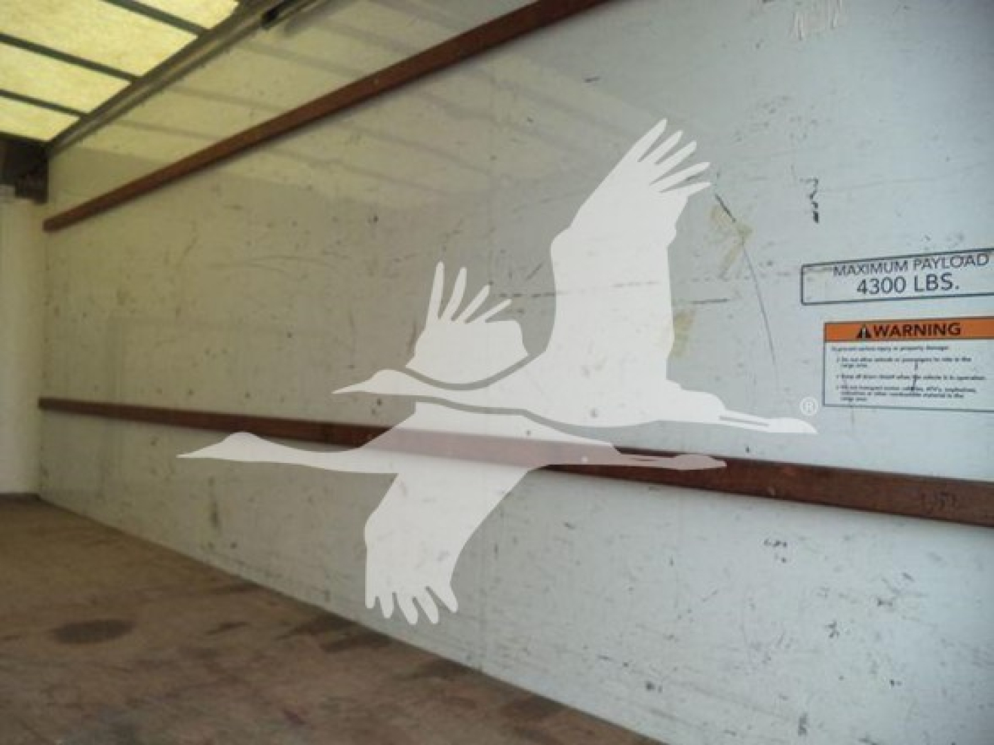 Truck trailer interior side with stenciled seagull graphic and warning label reading 'MAXIMUM PAYLOAD 4300 LBS' on the wall.