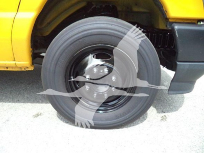 Ford E-350 front wheel and tire well view with yellow body panel; wheel shows steel rim and hub. Partial front fender and bumper visible.