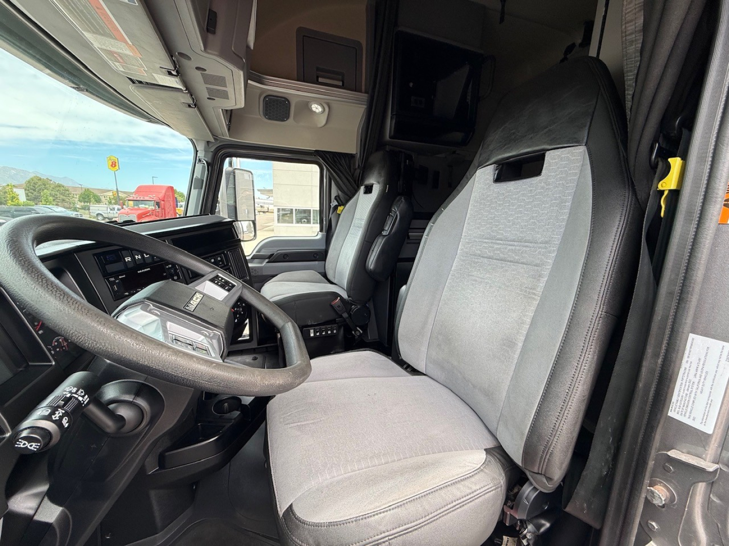 Semi truck interior showing driver seat and passenger seat with steering wheel, dashboard, and overhead sleeper area in a Mack Anthem.