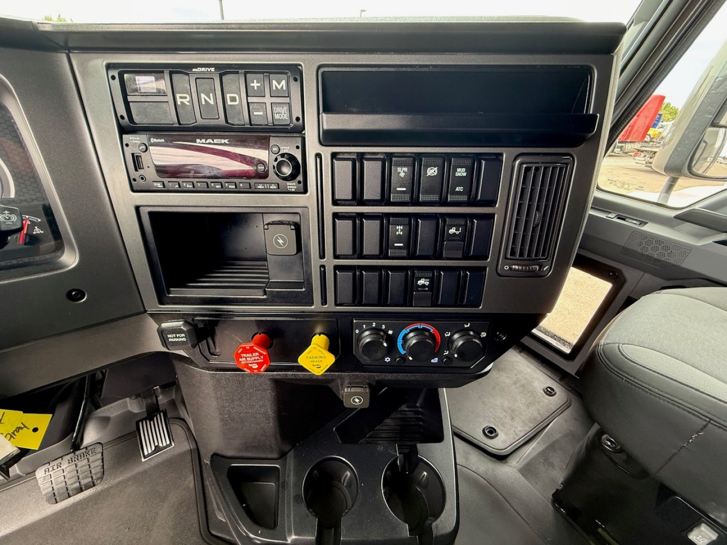 Dashboard of a Mack truck showing gear selector, radio, climate controls, and various switches in the cab interior.