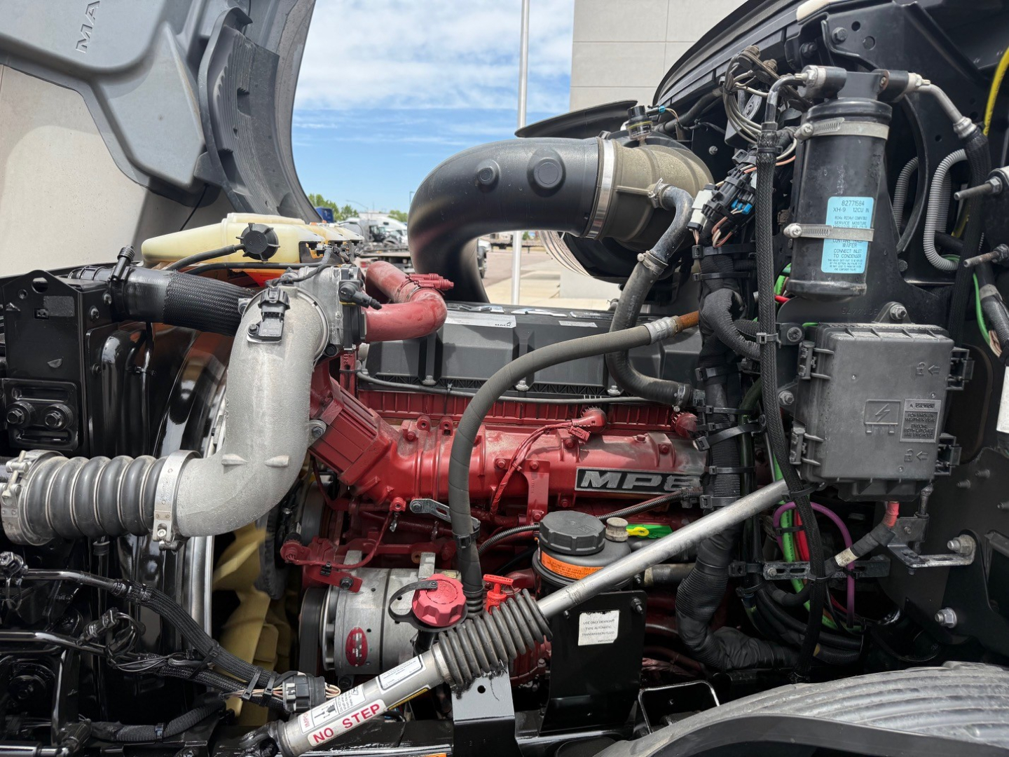 Mack ANTHEM engine bay with red engine block and surrounding components including hoses, air intake, and black plastic reservoir caps.