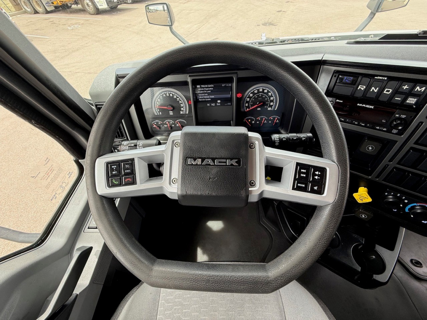 Mack vehicle cabin: steering wheel with 'MACk' emblem, dashboard with gauges, digital screen, and control panels visible.