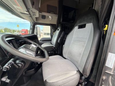 Semi truck interior showing driver seat and passenger seat with steering wheel, dashboard, and overhead sleeper area in a Mack Anthem.