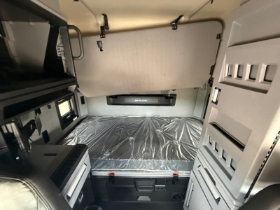 Truck cab sleeper interior with a platform bed in the rear wall, side storage, and control panels. Visible text includes MAHEN or MA KOM? on the bed shield and a small label on the dashboard area.