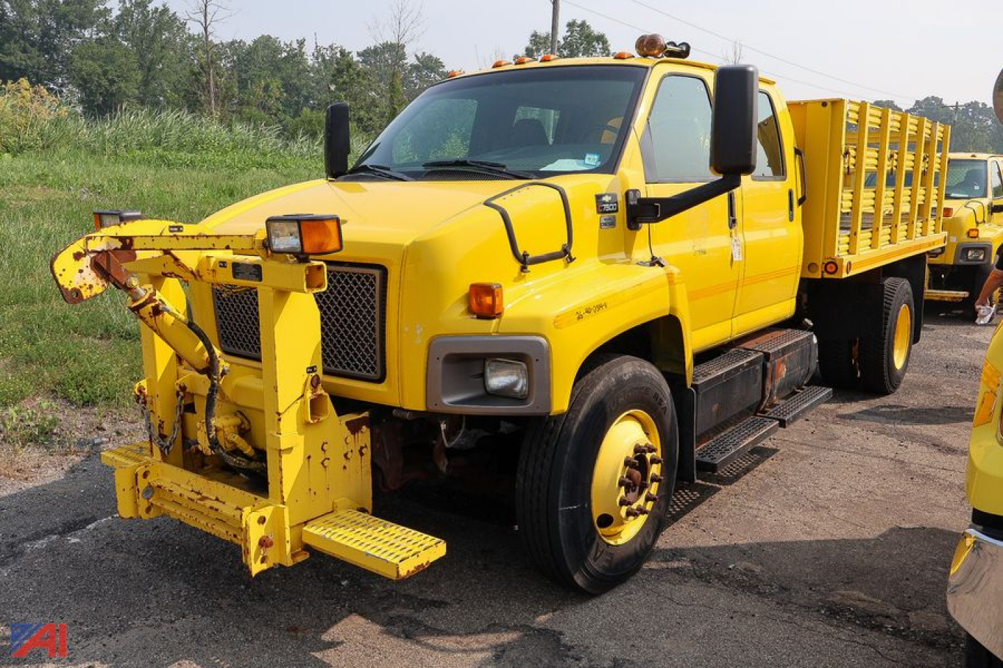 Front view of a yellow 2009 Chevrolet Kodiak C7500 crew cab stake truck with a front-mounted utility crane and stake bed.