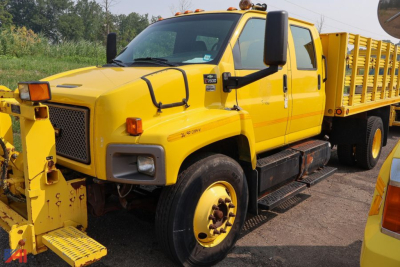 Chevrolet Kodiak C7500 crew cab stake truck with yellow paint and dual rear wheels, side steps, and stake bed visible.
