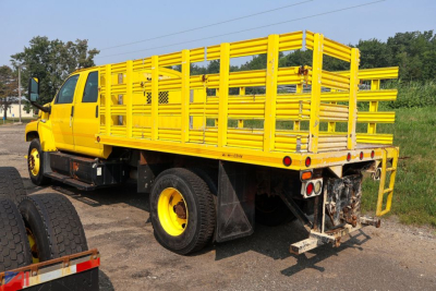 Chevrolet Kodiak C7500 crew cab stake truck with bright yellow stake bed and rear bumper area.