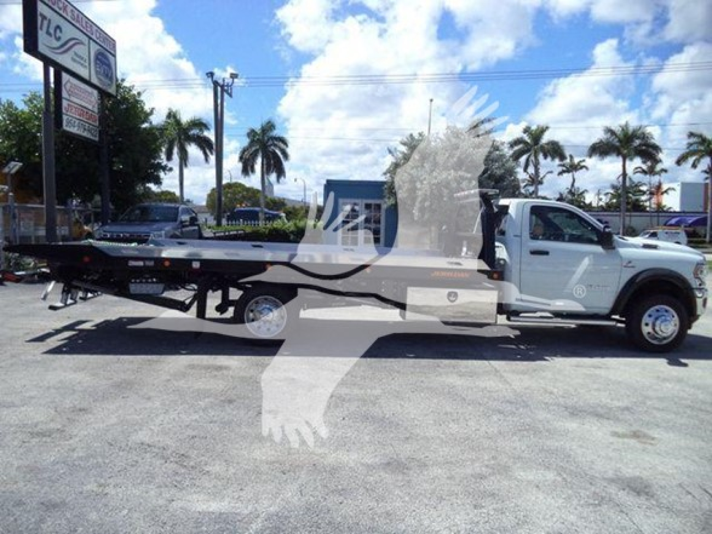 Ram 5500 rollback tow truck shown in side profile with flatbed and white cab; dealership lot in background with palm trees.