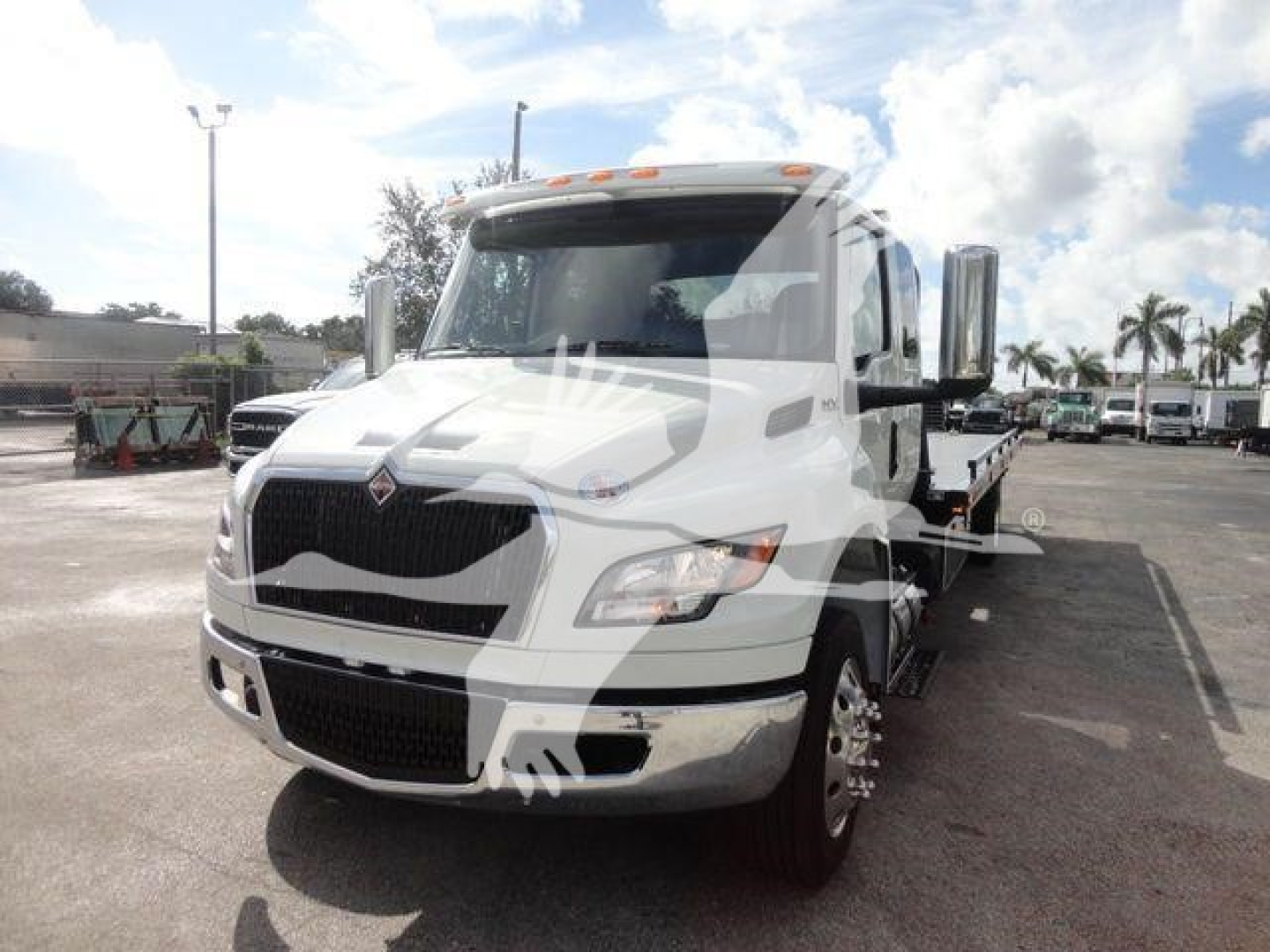 White 2027 International MV rollback tow truck front view with black grille and chrome bumper, cab interior visible, dealership lot in background.