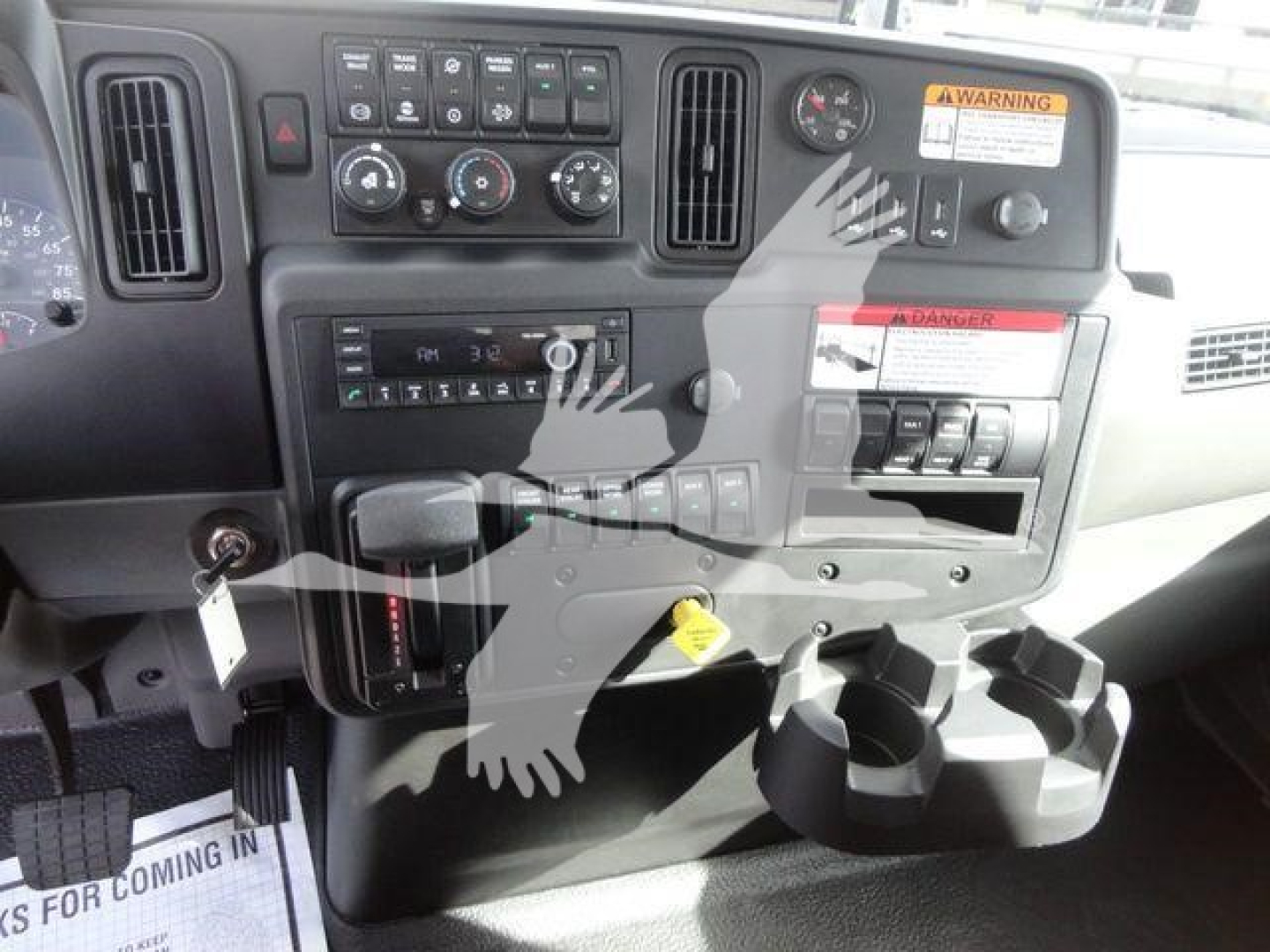 Dashboard of a truck cab showing control panel, vents, warning label, cup holders, and gear shifter area with numerous dials and switches.
