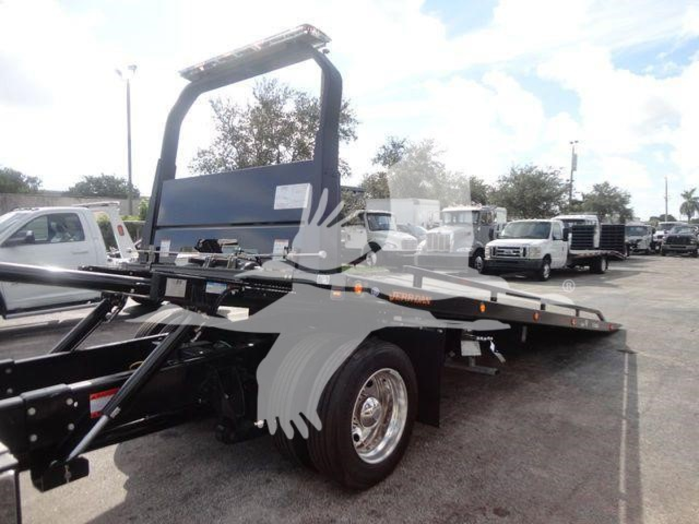 Trailer truck with a flatbed/rollback showing a tall blue cab guard and rear wheel; no legible labels visible on the side in this view.