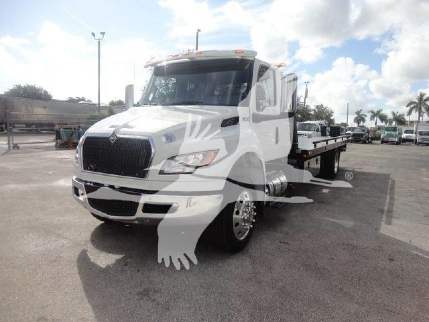 International MV rollback truck in white with flatbed on a dealership lot.