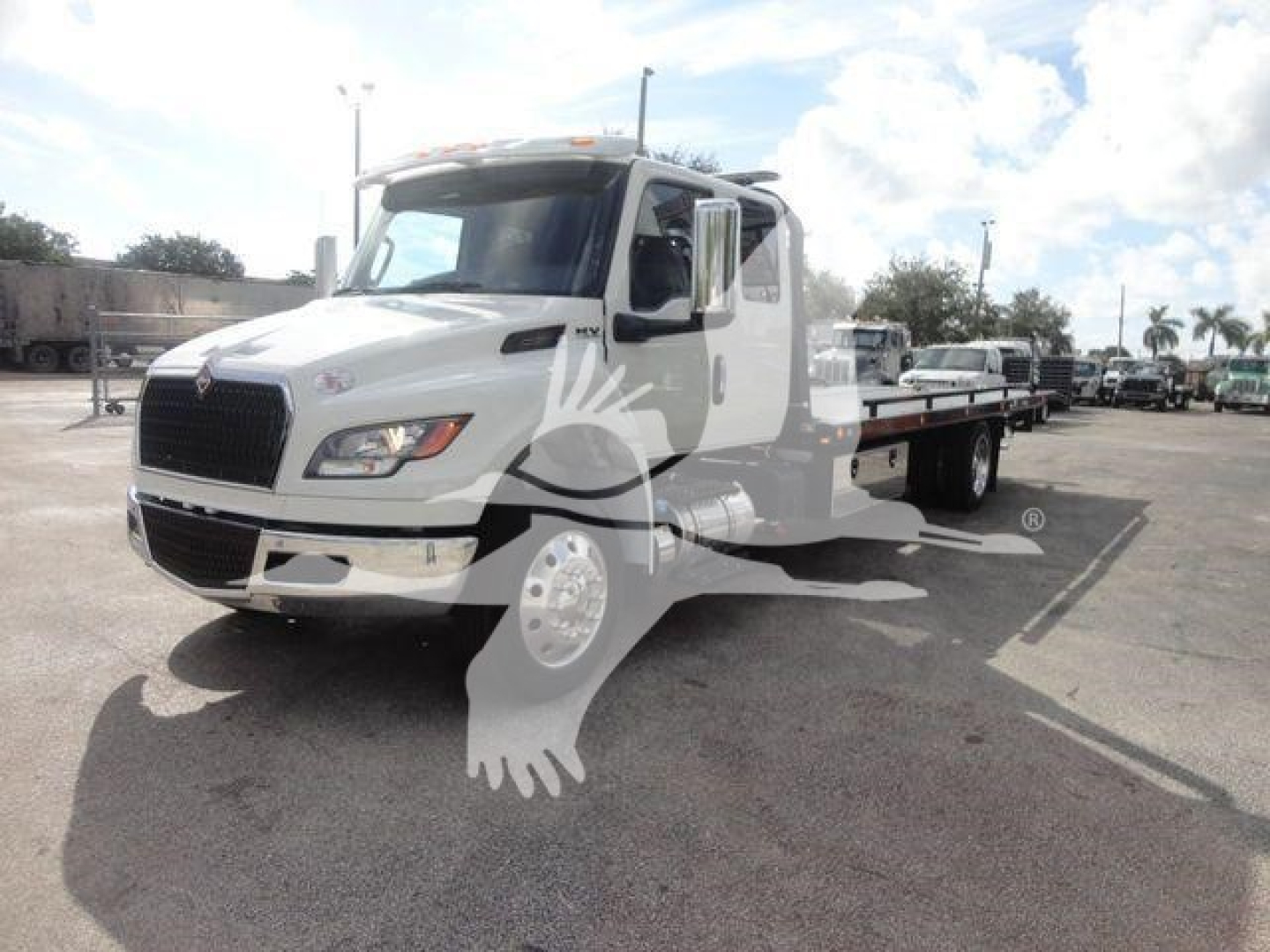 Flatbed tow truck from an angle showing front and left side of a white International MV with long flatbed and wheel lift in a dealership lot.