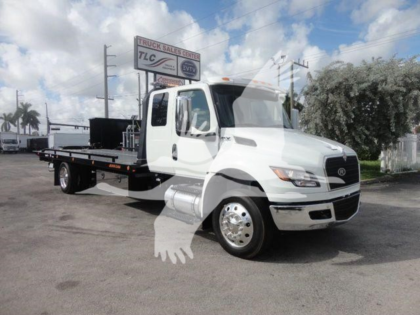Truck with flatbed tow body and International MV cab showing large front grille and rounded headlights.