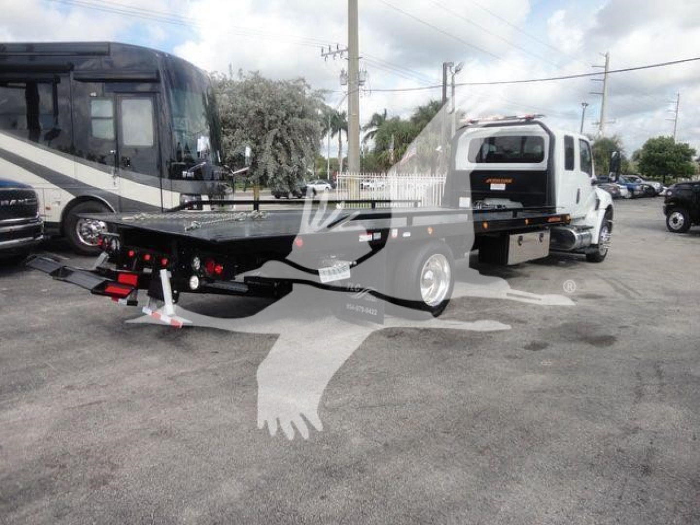 Flatbed tow truck in a dealership lot showing MV607EXCAB22XLP International MV chassis and trailer bed with side rails.